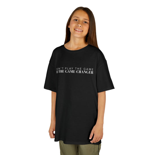 A smiling young girl with long brown hair and brown eyes wearing khaki pants and a kid's short sleeve black t-shirt with white letters that say don't play the game be the game-changer across the chest
