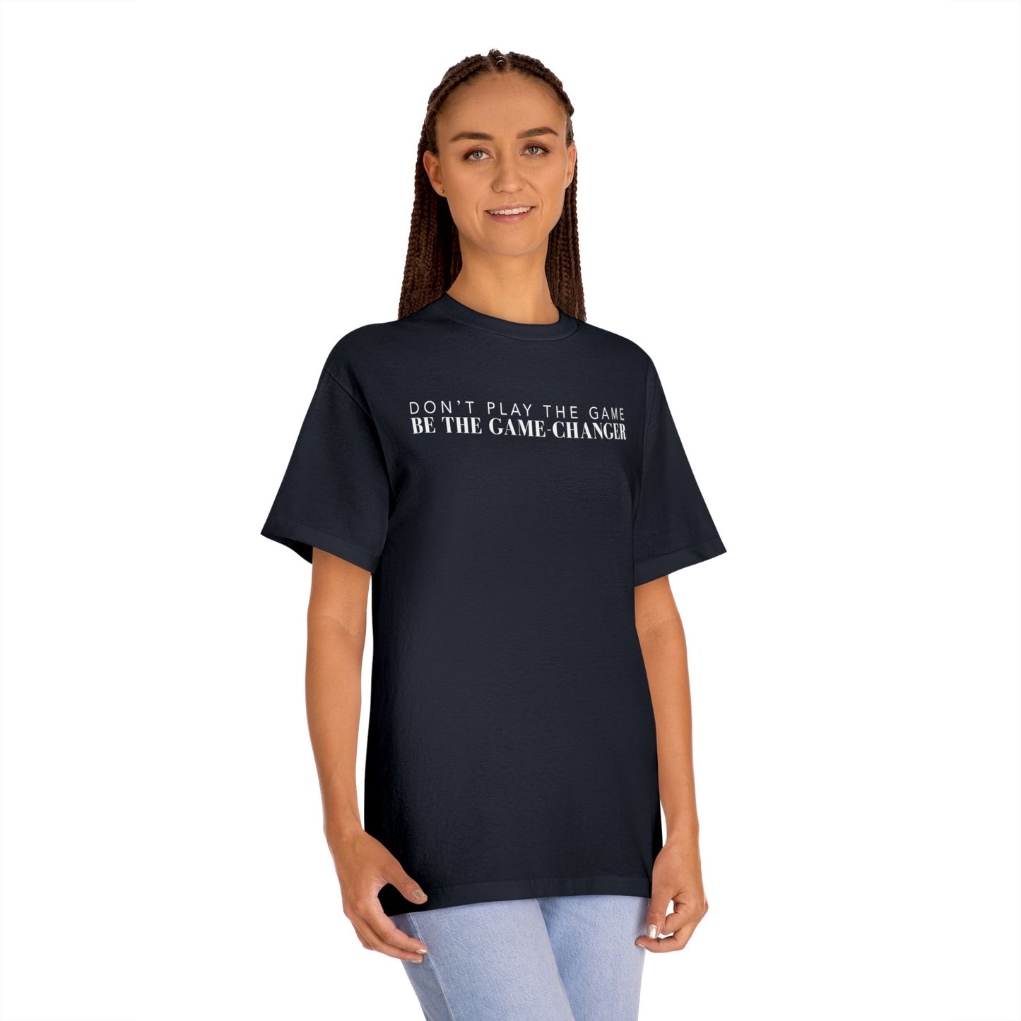 A smiling woman with green eyes and brown braids wearing light blue jeans and a short sleeve black t-shirt with white letters that say don't play the game be the game-changer across the chest