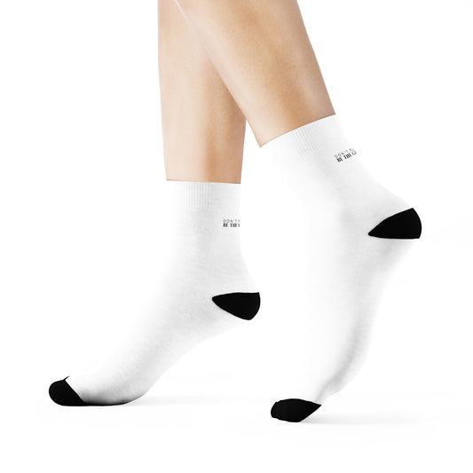 a side view of a pair of legs from the calf down standing on their toes wearing white socks with black accents on the toes and heel and black text on the back and bottom of the sock that says don't play the game be the game-changer