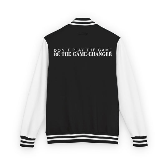 A view of the back of a varsity jacket with white leather sleeves with black and white striped accents, a black fabric body with black and white striped accents on the collar and bottom of the jacket with don't play the game be the game-changer written in white text across the back of the shoulders