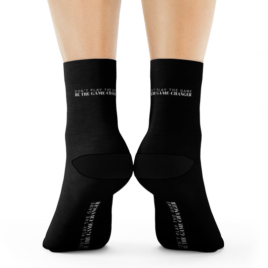 a view from behind of a pair of legs from the calf down standing on their toes wearing black socks with black accents on the toes and heel and black text on the back and bottom of the sock that says don't play the game be the game-changer