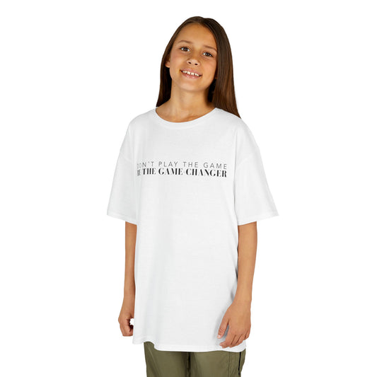 A smiling young girl with long brown hair and brown eyes wearing khaki pants and a kid's short sleeve white t-shirt with black letters that say don't play the game be the game-changer across the chest