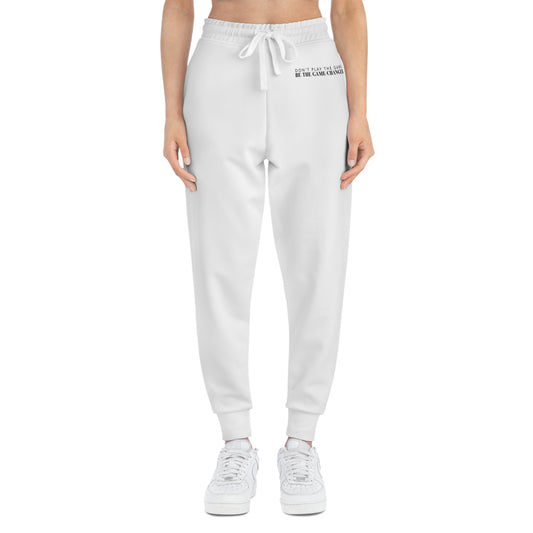 A front view of a woman from the belly button down wearing white sneakers and white joggers with a white draw string and don't play the game be the game-changer written in small black text across the left hip below the waistband