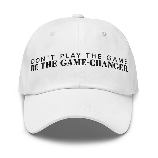 Photo of a white baseball cap that has  black embroidered letters saying don't play the game be the game changer