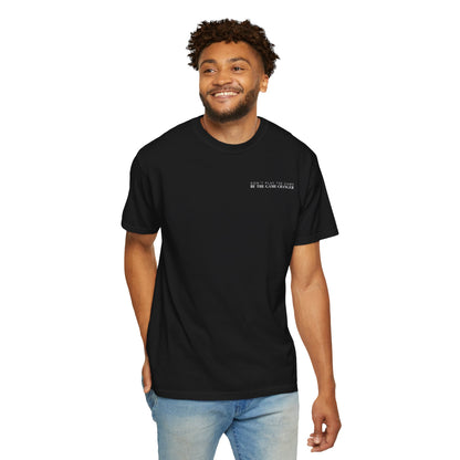 A smiling man with short curly brown hair, dark eyes, and facial hair wearing light wash jeans and a short sleeve black t-shirt with white letters that say don't play the game be the game-changer across the left chest