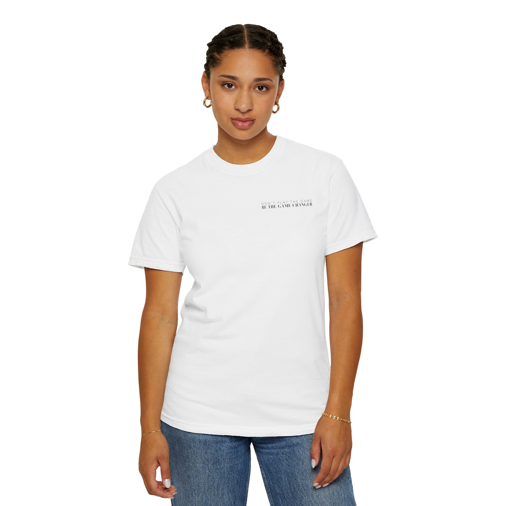 A confident looking woman with dark pulled back hair in braids and dark eyes wearing gold hoop earrings, a gold bracelet, medium wash jeans, and a short sleeve white t-shirt with black letters that say don't play the game be the game-changer across the left chest