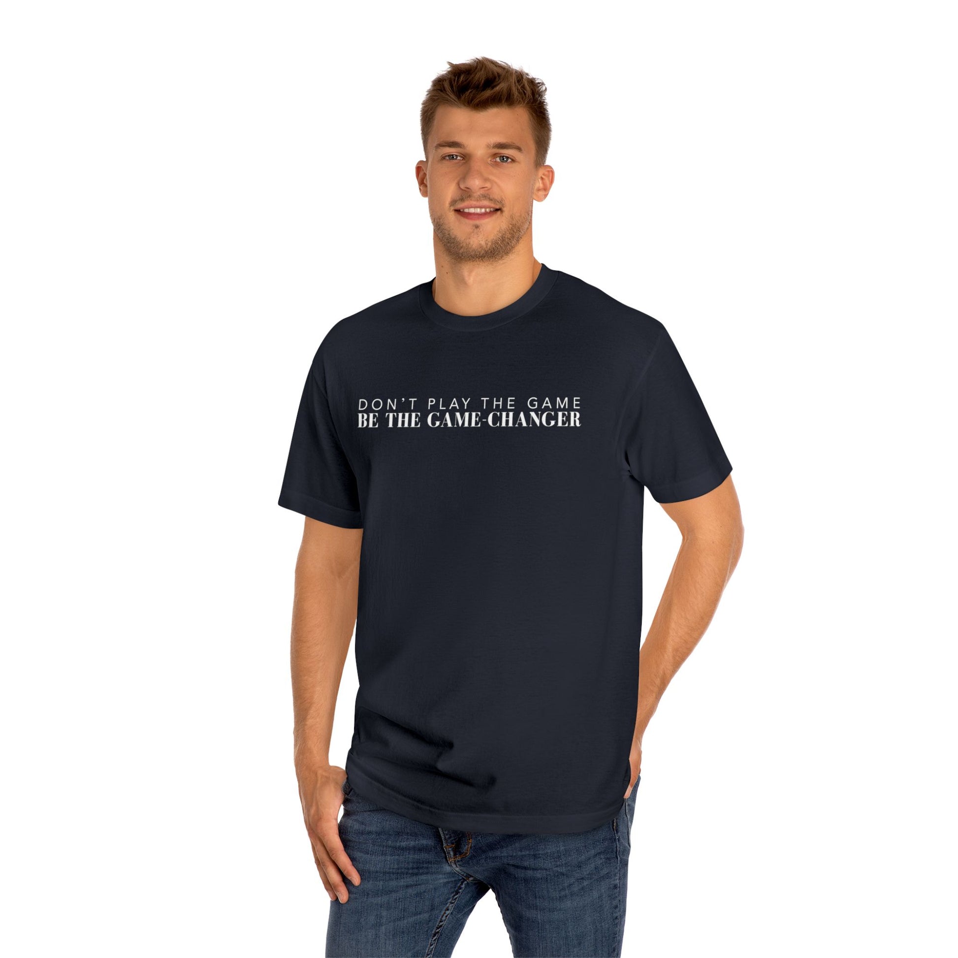 A smiling man with green eyes and short brown hair wearing dark blue jeans and a short sleeve black t-shirt with white letters that say don't play the game be the game-changer across the chest
