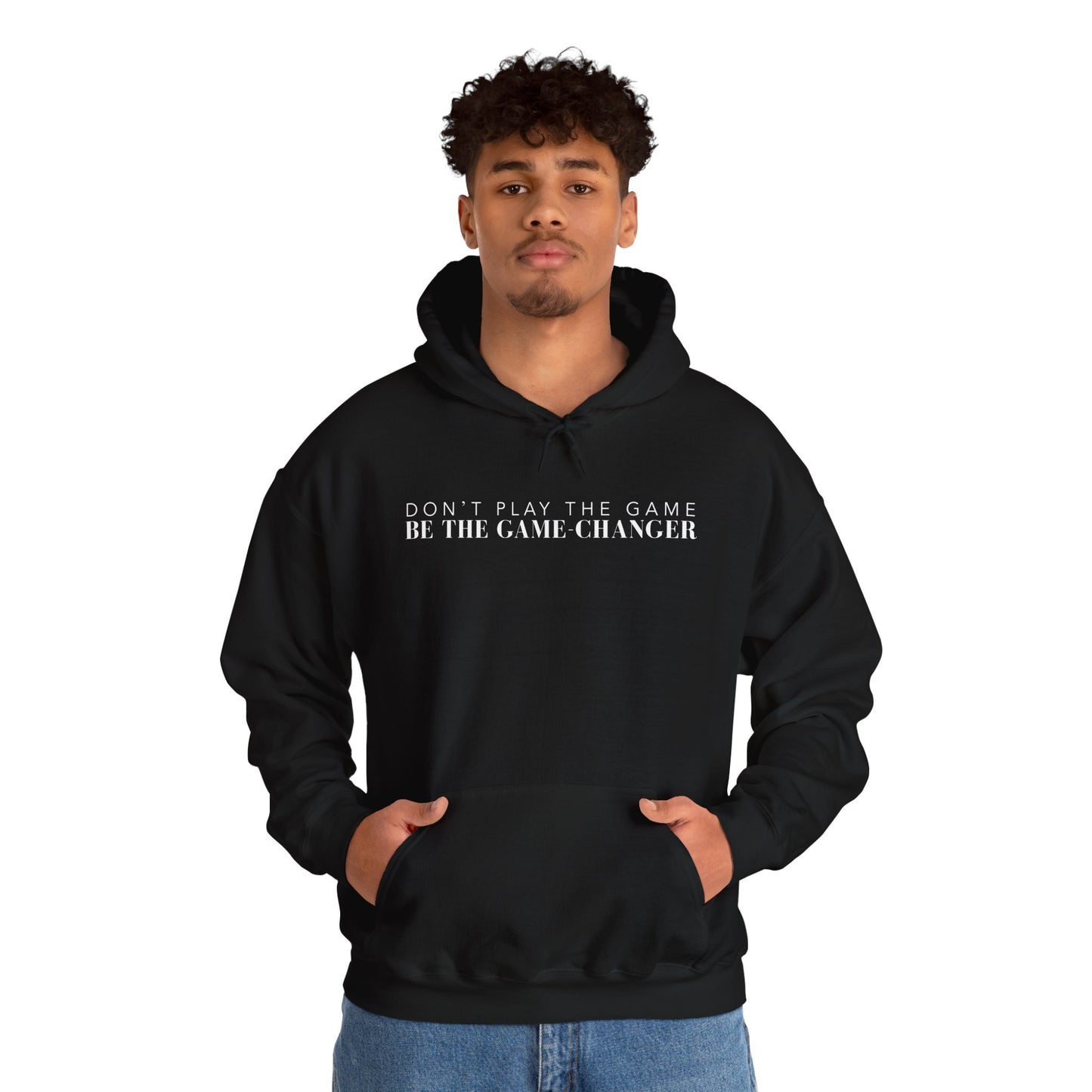 A confident looking man with dark eyes and dark curly hair wearing black hoodie with draw strings, a kangaroo pocket, and white letters that say don't play the game be the game-changer across the chest