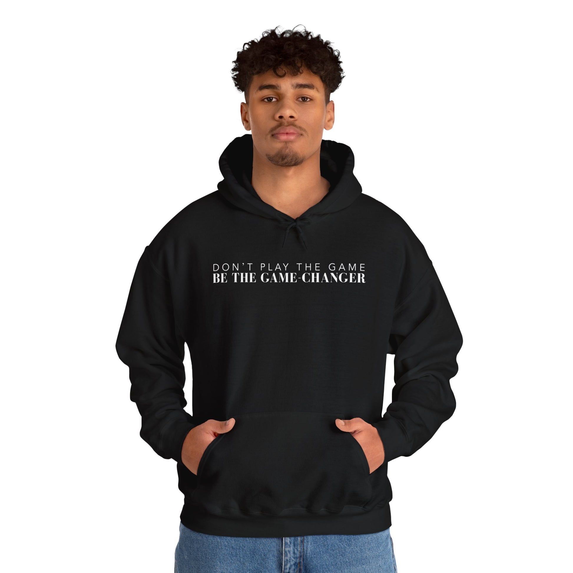 A confident looking man with dark eyes and dark curly hair wearing black hoodie with draw strings, a kangaroo pocket, and white letters that say don't play the game be the game-changer across the chest