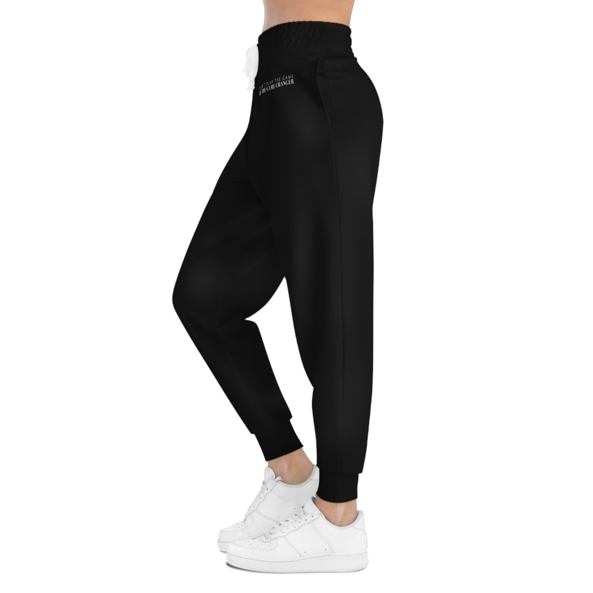 A side view of a woman from the belly button down wearing white sneakers and black joggers with a white draw string and don't play the game be the game-changer written in small white text across the left hip below the waistband