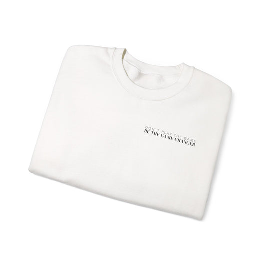 A folded cozy white crewneck sweater with black letters that say don't play the game be the game-changer over the left chest 
