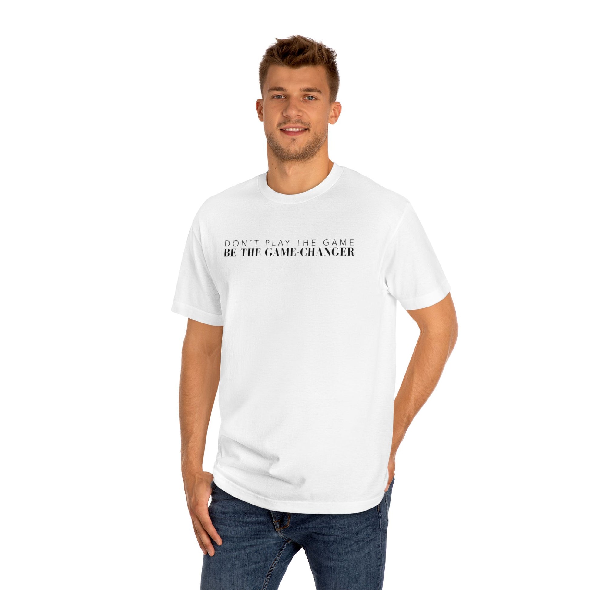 A smiling man with green eyes and short brown hair wearing dark blue jeans and a short sleeve black t-shirt with white letters that say don't play the game be the game-changer across the chest