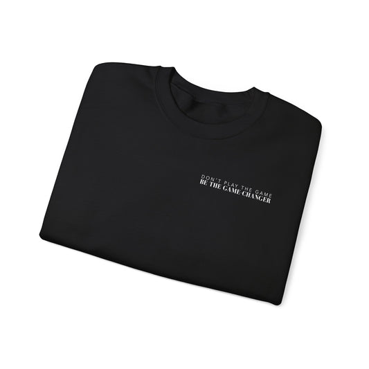A folded cozy black crewneck sweater with white letters that say don't play the game be the game-changer over the left chest 