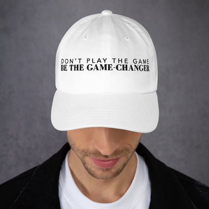 Photo of a man looking down and wearing a white baseball cap that has  black embroidered letters saying don't play the game be the game changer