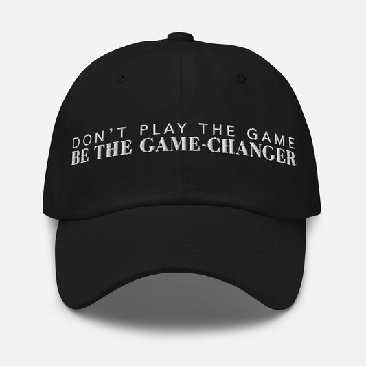 Photo of a black baseball cap that has white embroidered letters saying don't play the game be the game changer on a white background