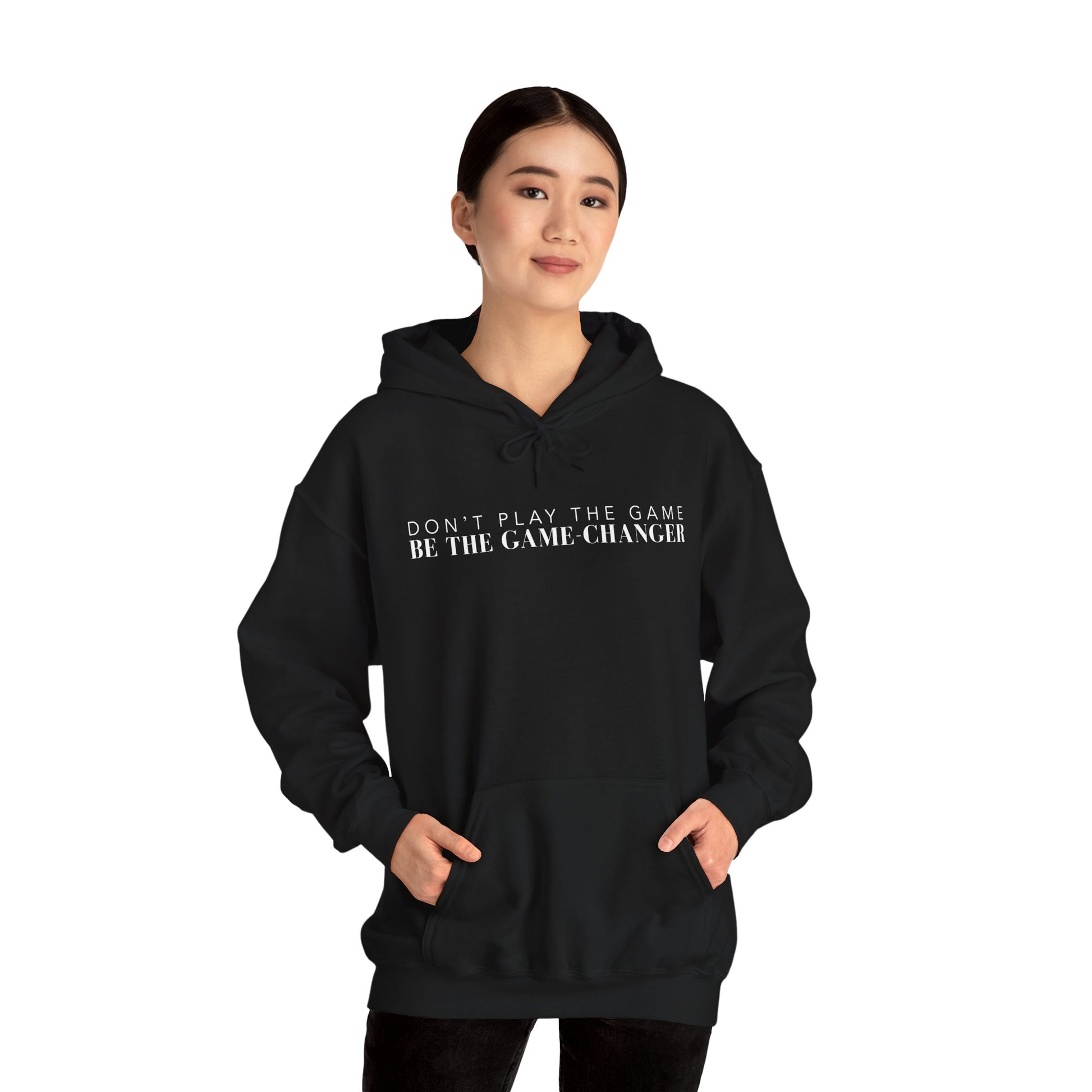 A smiling woman with dark hair and dark eyes wearing a black hoodie with draw strings, a kangaroo pocket, and white letters that say don't play the game be the game-changer across the chest