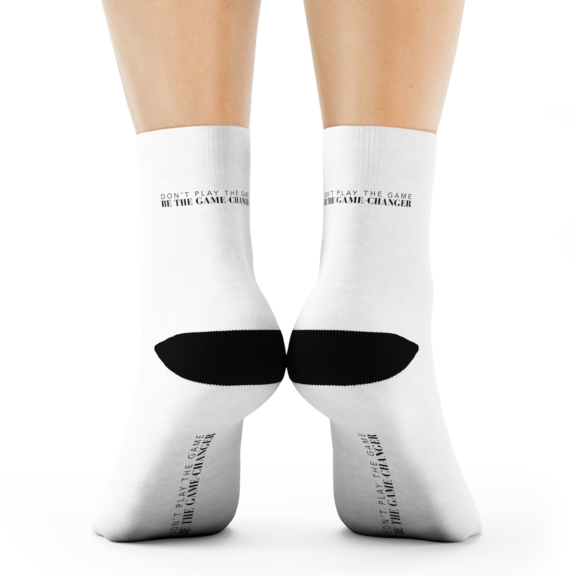 a back view of a pair of legs from the calf down white socks with black accents on the toes and heel and black text on the back and bottom of the sock that says don't play the game be the game-changer
