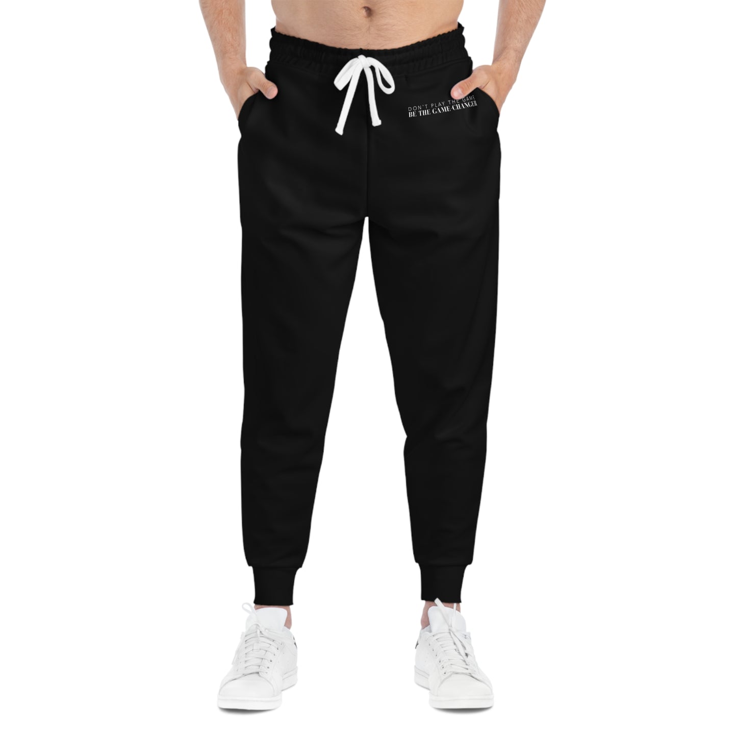 A front view of a man from the belly button down wearing white sneakers and black joggers with a white draw string and don't play the game be the game-changer written in small white text across the left hip below the waistband