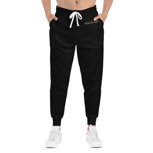 A front view of a man from the belly button down wearing white sneakers and black joggers with a white draw string and don't play the game be the game-changer written in small white text across the left hip below the waistband