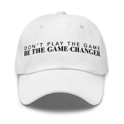 Photo of a white baseball cap that has  black embroidered letters saying don't play the game be the game changer
