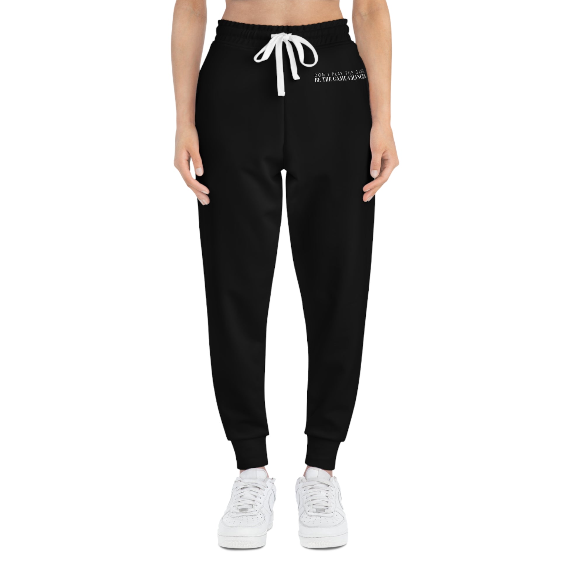 A front view of a woman from the belly button down wearing white sneakers and black joggers with a white draw string and don't play the game be the game-changer written in small white text across the left hip below the waistband