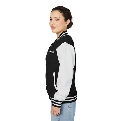 The side view of a smiling woman with dark curly hair pulled back into a bun and dark eyes wearing light colored blue jeans and a varsity jacket with white leather sleeves with black and white striped accents, a black fabric body with black and white striped accents on the collar and bottom of the jacket and white pockets and buttons with don't play the game be the game-changer written in white text across the left chest 