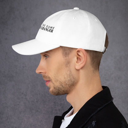Photo of a man looking to the left and wearing a white baseball cap that has  black embroidered letters saying don't play the game be the game changer